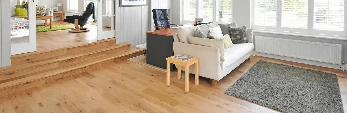 A modern living room with professionally installed laminate flooring, a beige sofa, a small side table, a gray rug, and large windows with white shutters in Knoxville, TN